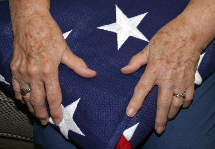 elderly woman's hands holding her husband's American flag after his funeral.