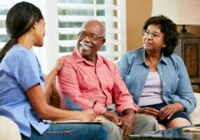 Nurse Making Notes During Home Visit With Senior Couple